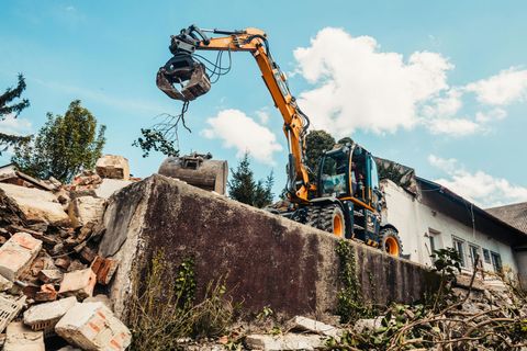 Excavator demolishing a concrete structure amid rubble under a bright sky