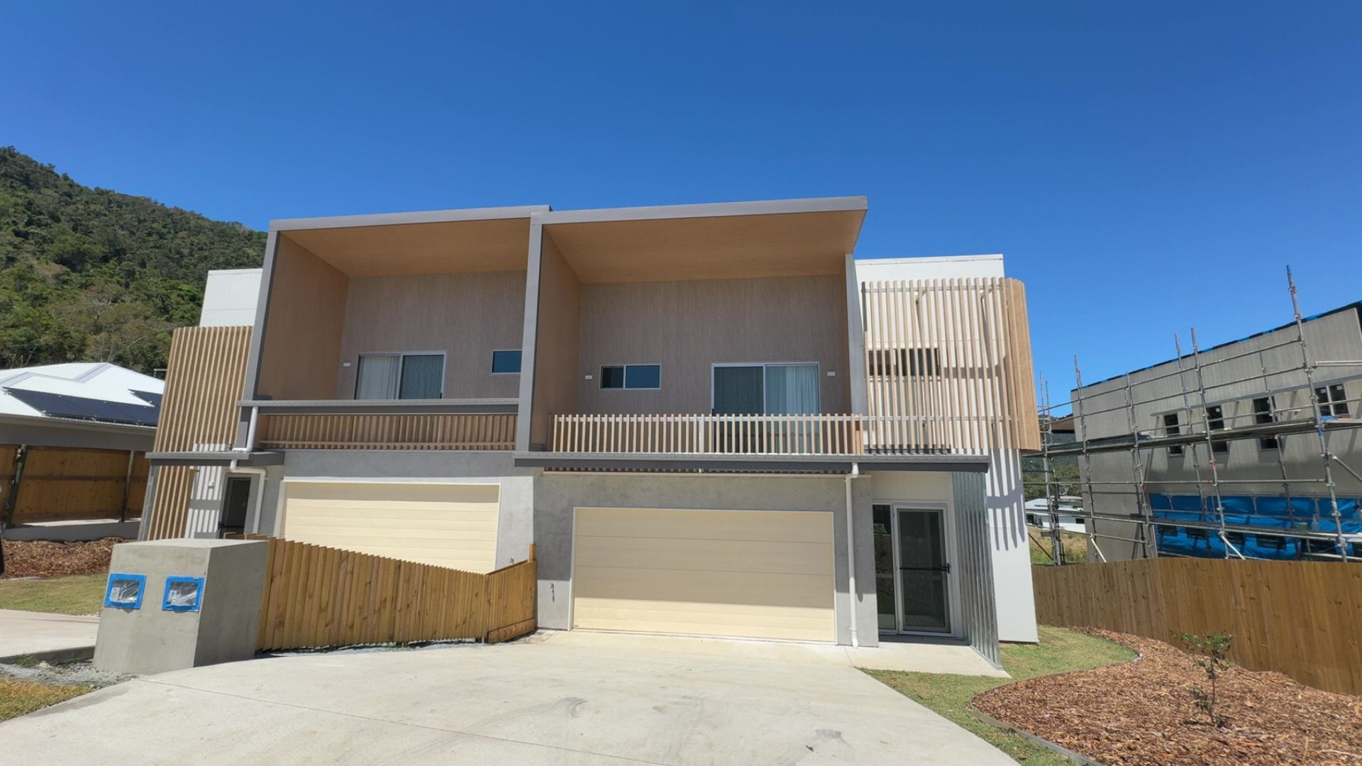 Modern two-story apartment building with garage doors, balconies, and a clear blue sky — Coral Coast Building & Management in Cannon Valley, QLD