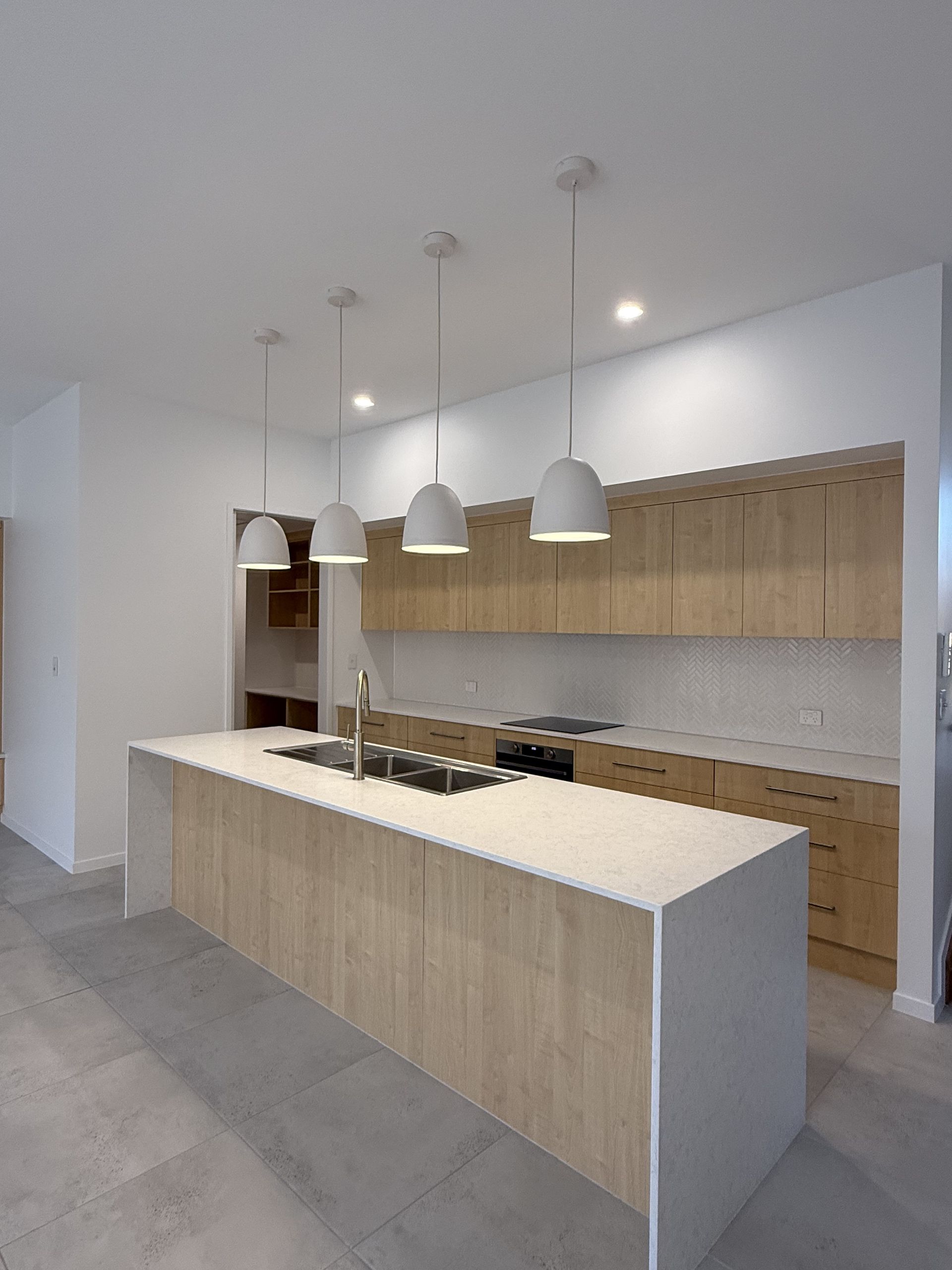 Modern kitchen with a long island, pendant lights, and wood cabinetry in a bright open space — Coral Coast Building & Management in Cannon Valley, QLD