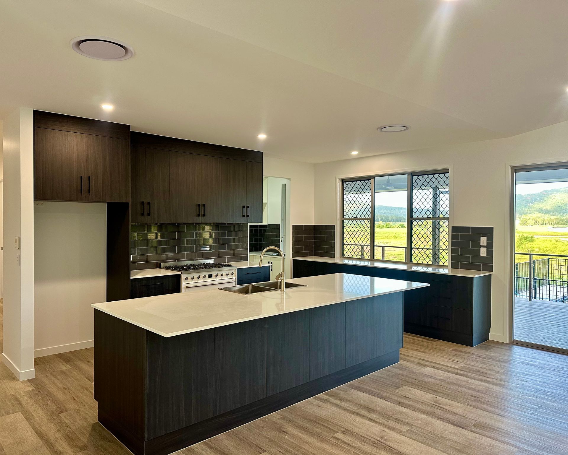 Modern kitchen with dark cabinets, large island, and bright open dining area with sliding glass doors — Coral Coast Building & Management in Cannon Valley, QLD 