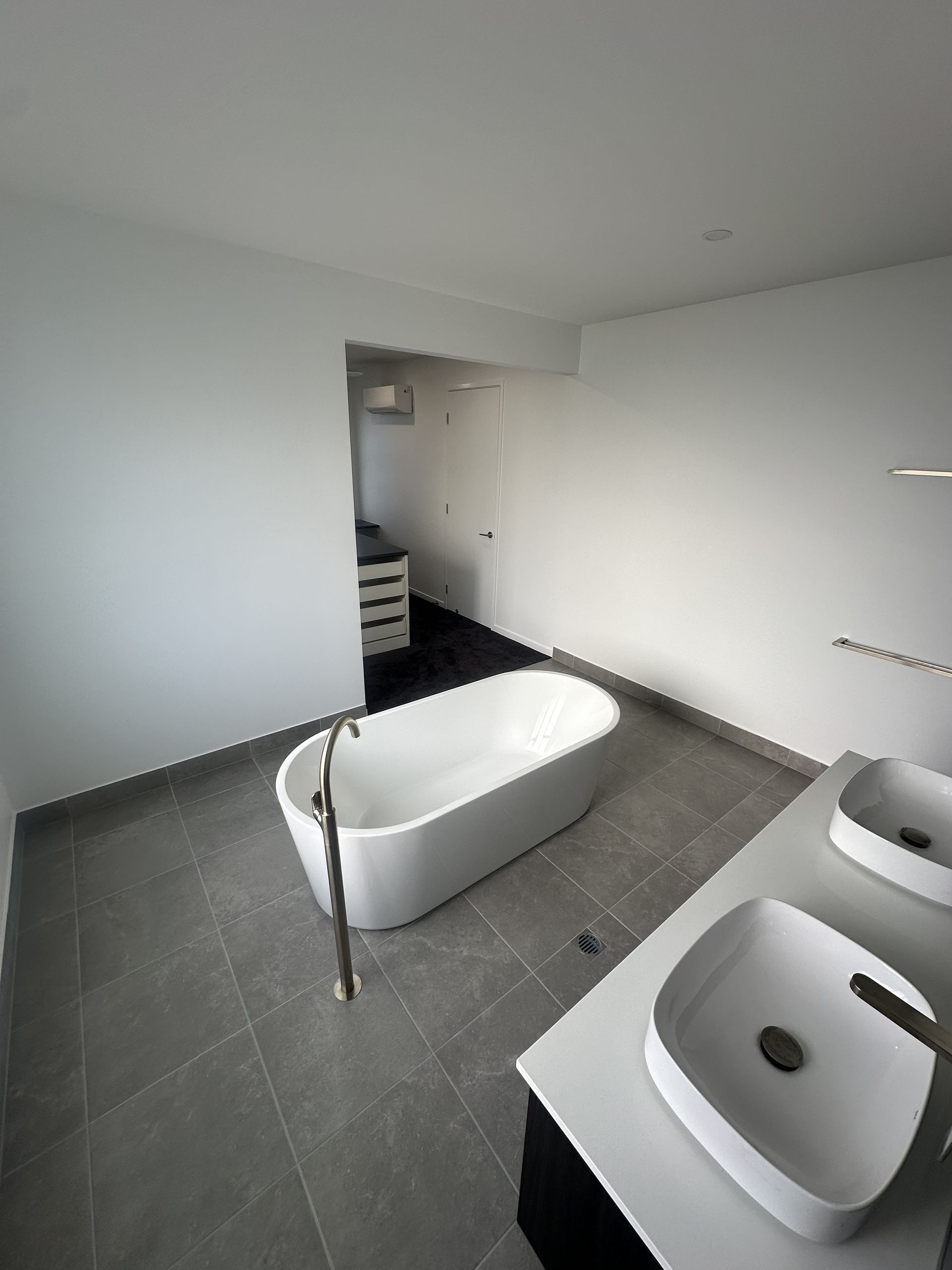 Minimalist white bathroom with a freestanding tub, sink, and grey tile floor, viewed from the doorway — Coral Coast Building & Management in Cannon Valley, QLD 