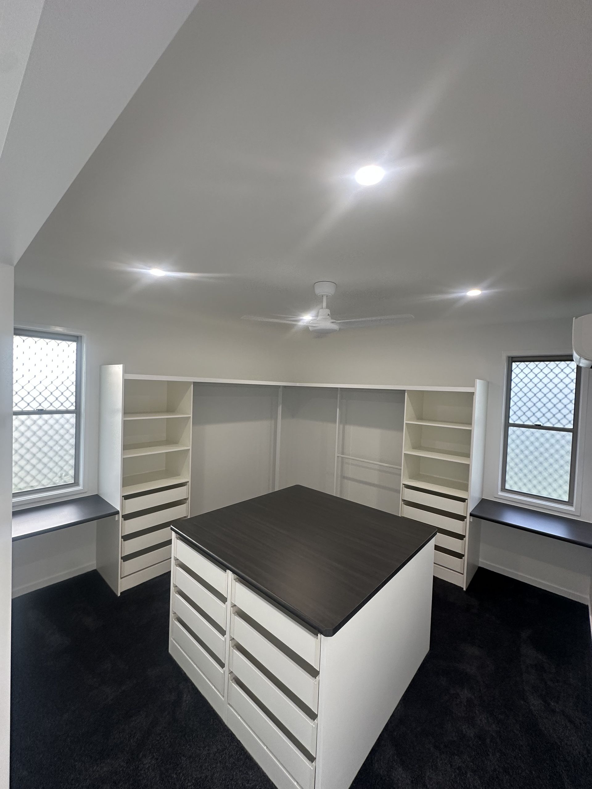 Spacious white walk-in closet with built-in shelves, drawers, and a central island under ceiling lights — Coral Coast Building & Management in Cannon Valley, QLD 