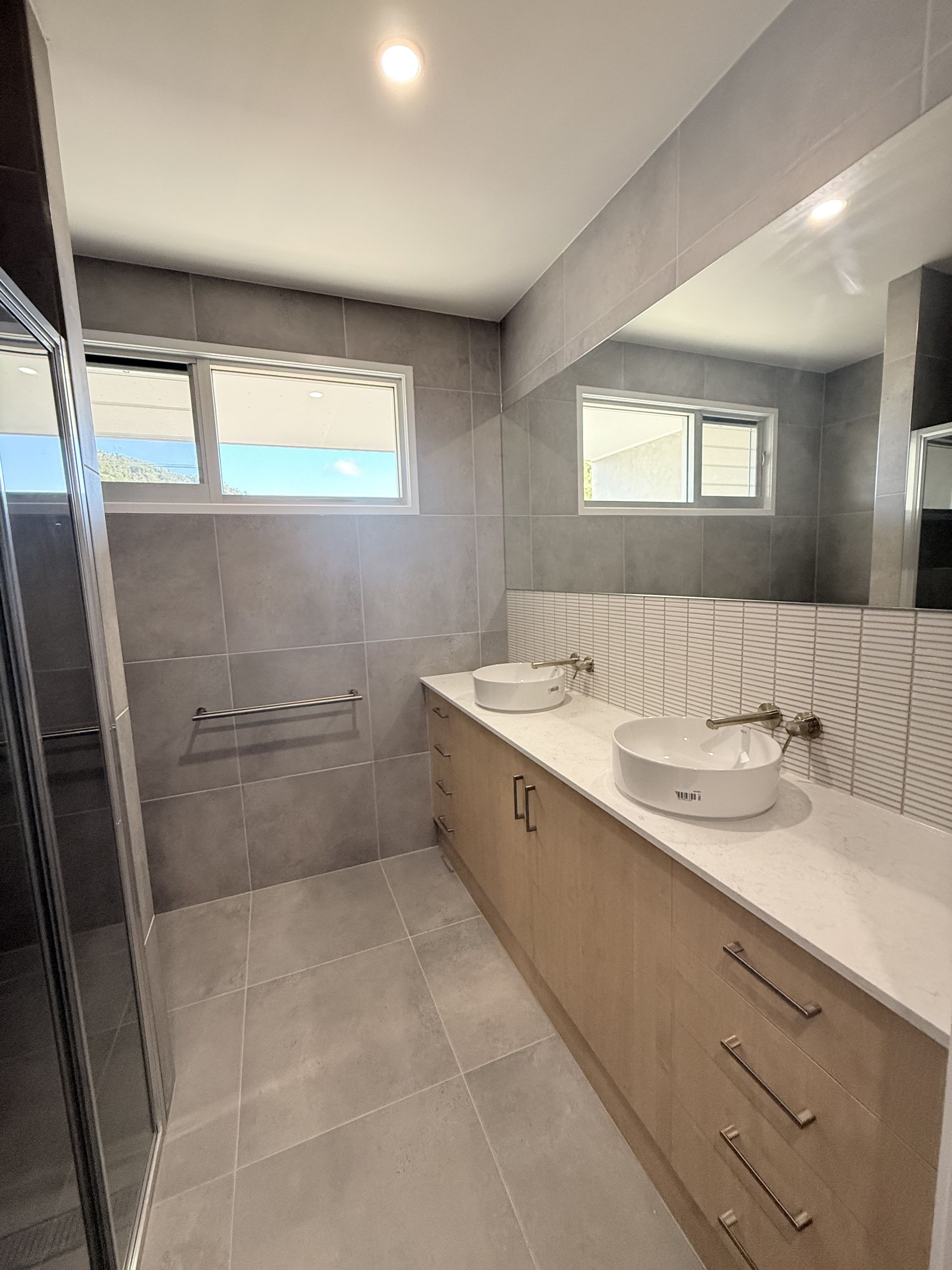 Modern bathroom with double sink vanity, large mirror, grey tiles, and a walk-in shower — Coral Coast Building & Management in Cannon Valley, QLD 