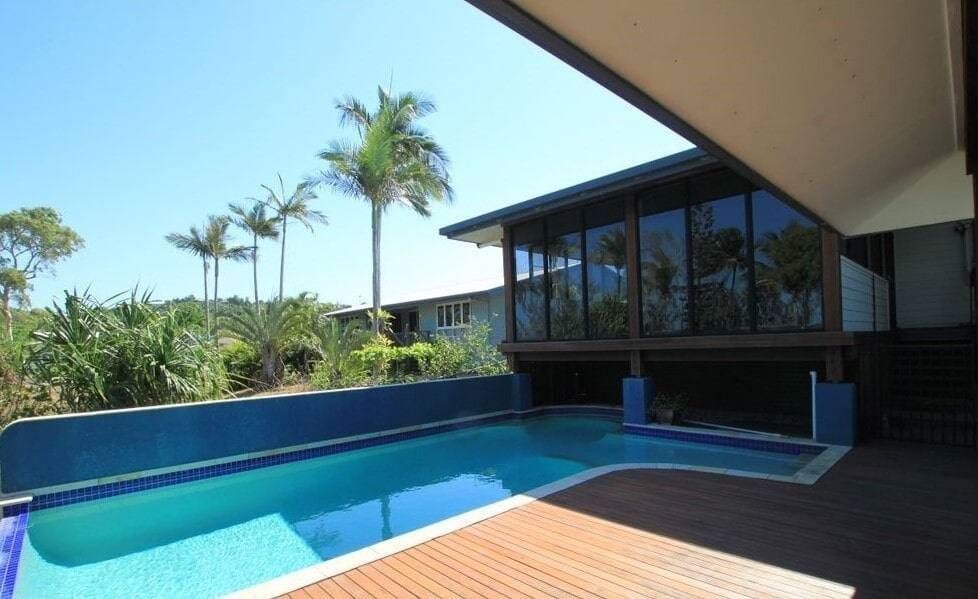 A Large Swimming Pool in Front of a House With Palm Trees — Coral Coast Building & Management in Cannon Valley, QLD