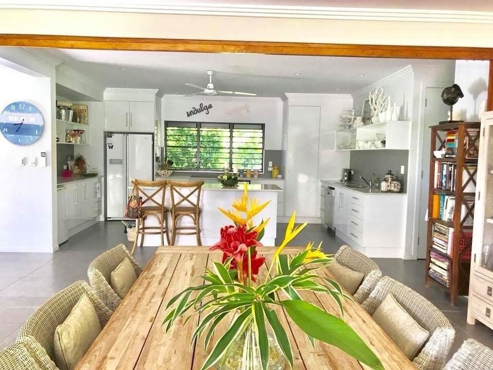 A Dining Room Table With a Vase of Flowers on It and a Kitchen in the Background — Coral Coast Building & Management in Cannon Valley, QLD