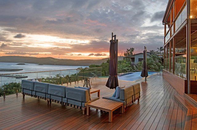 A Large Wooden Deck With a Couch and Umbrellas Overlooking a Lake at Sunset — Coral Coast Building & Management in Cannon Valley, QLD