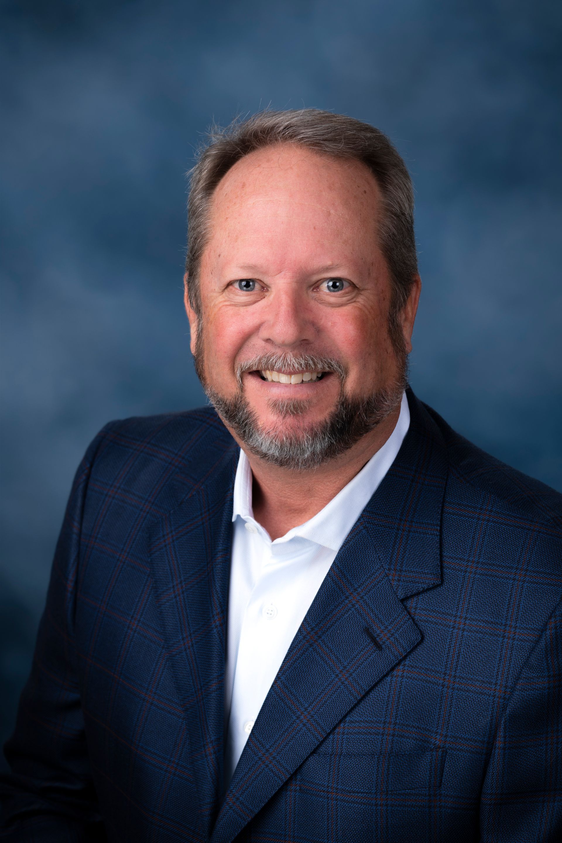 Smiling man in a navy blazer and white shirt against a blue studio backdrop
