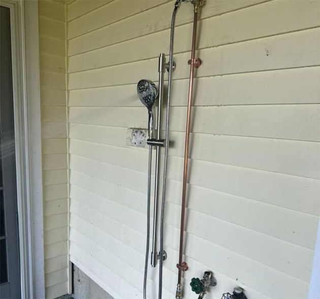 A shower head is attached to a wall with copper pipes