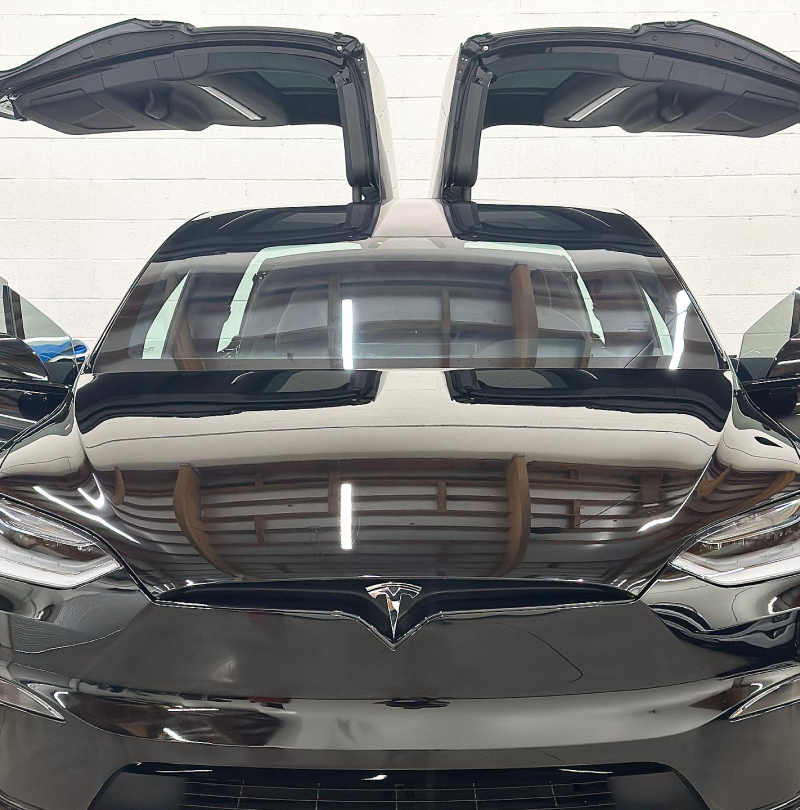 A black Tesla Model X shown from the front with its falcon-wing doors open inside a garage.
