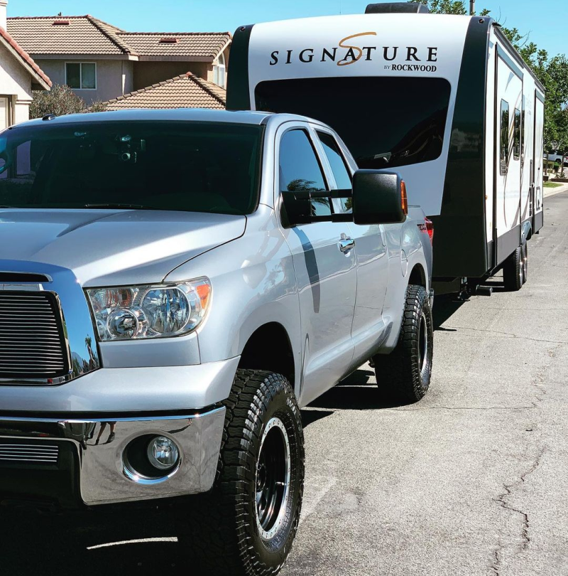 A silver truck is parked next to a signature trailer
