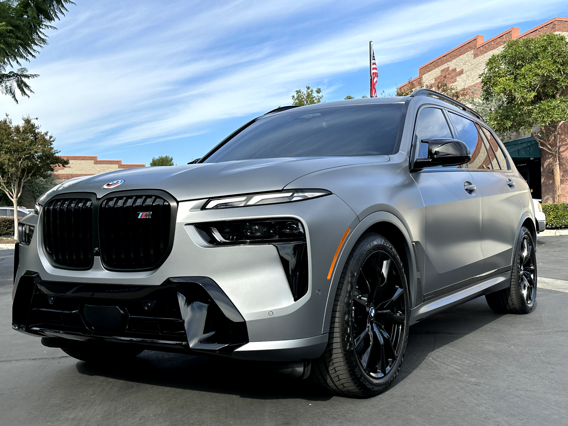Silver BMW SUV parked on a street, front three-quarter view with black rims and trees in the background