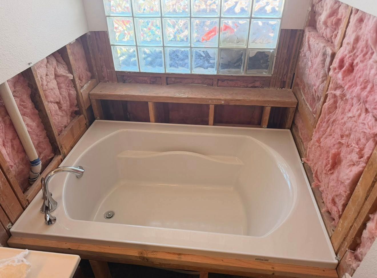 Bathtub under renovation with exposed insulation and unfinished wood framing around it