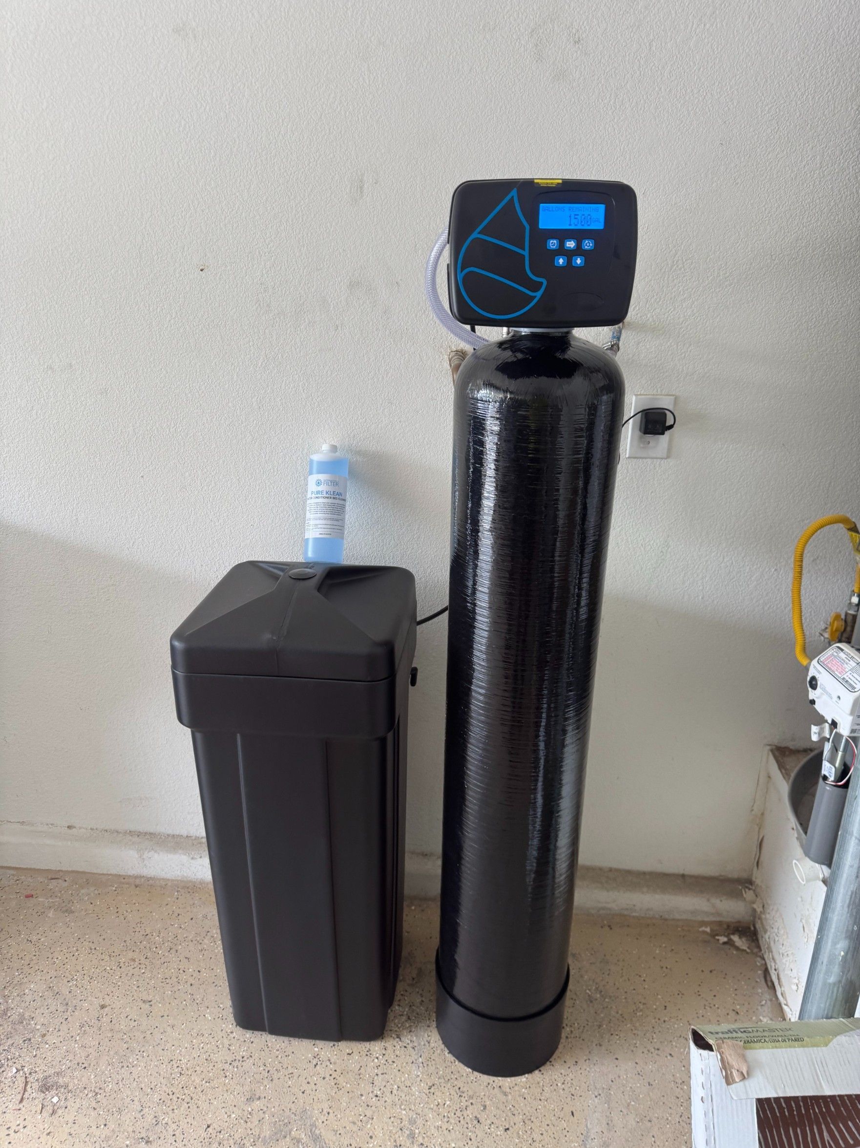 Black water softener tank and matching cabinet beside a wall with a small display on top.