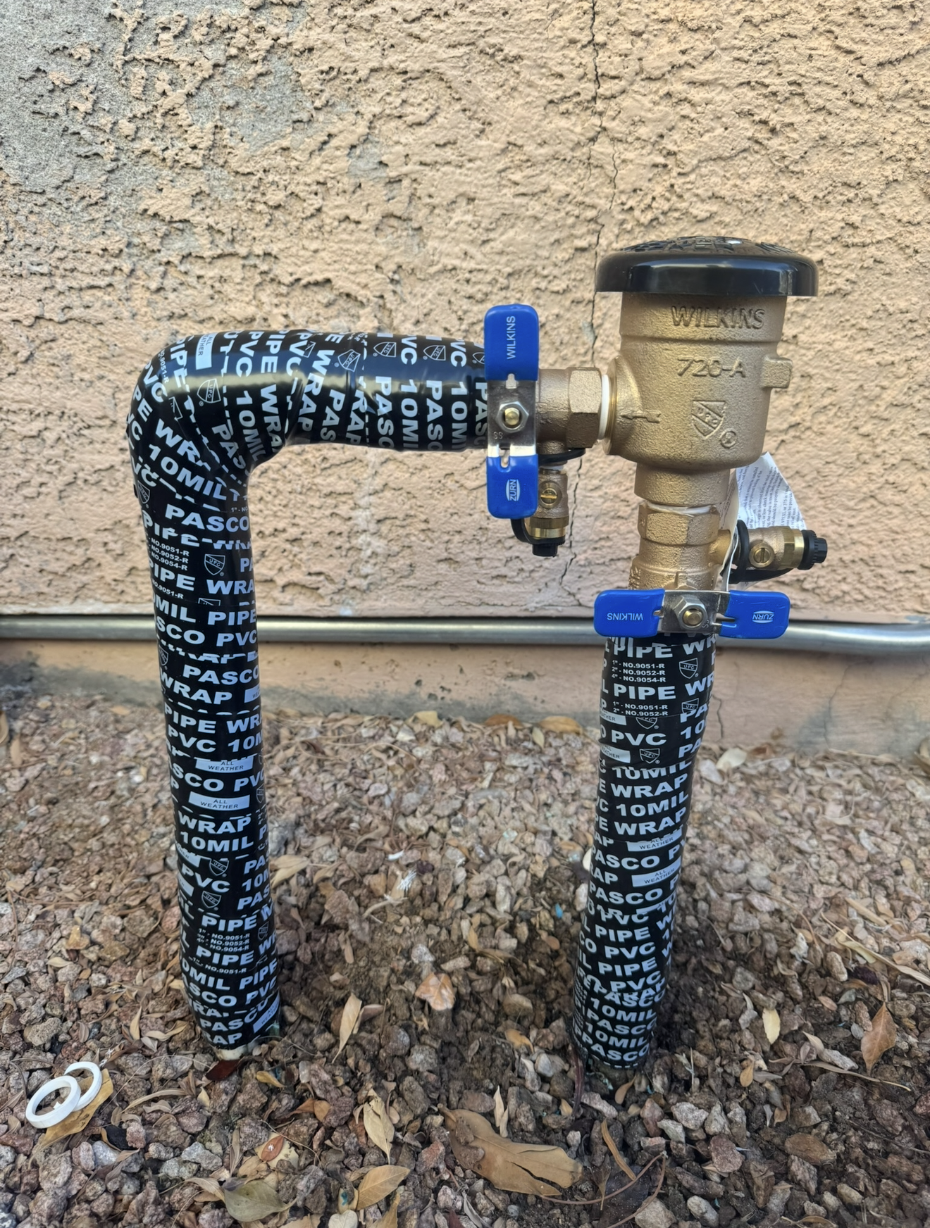 Gas meter with black insulated pipes and blue valves against a stucco wall.