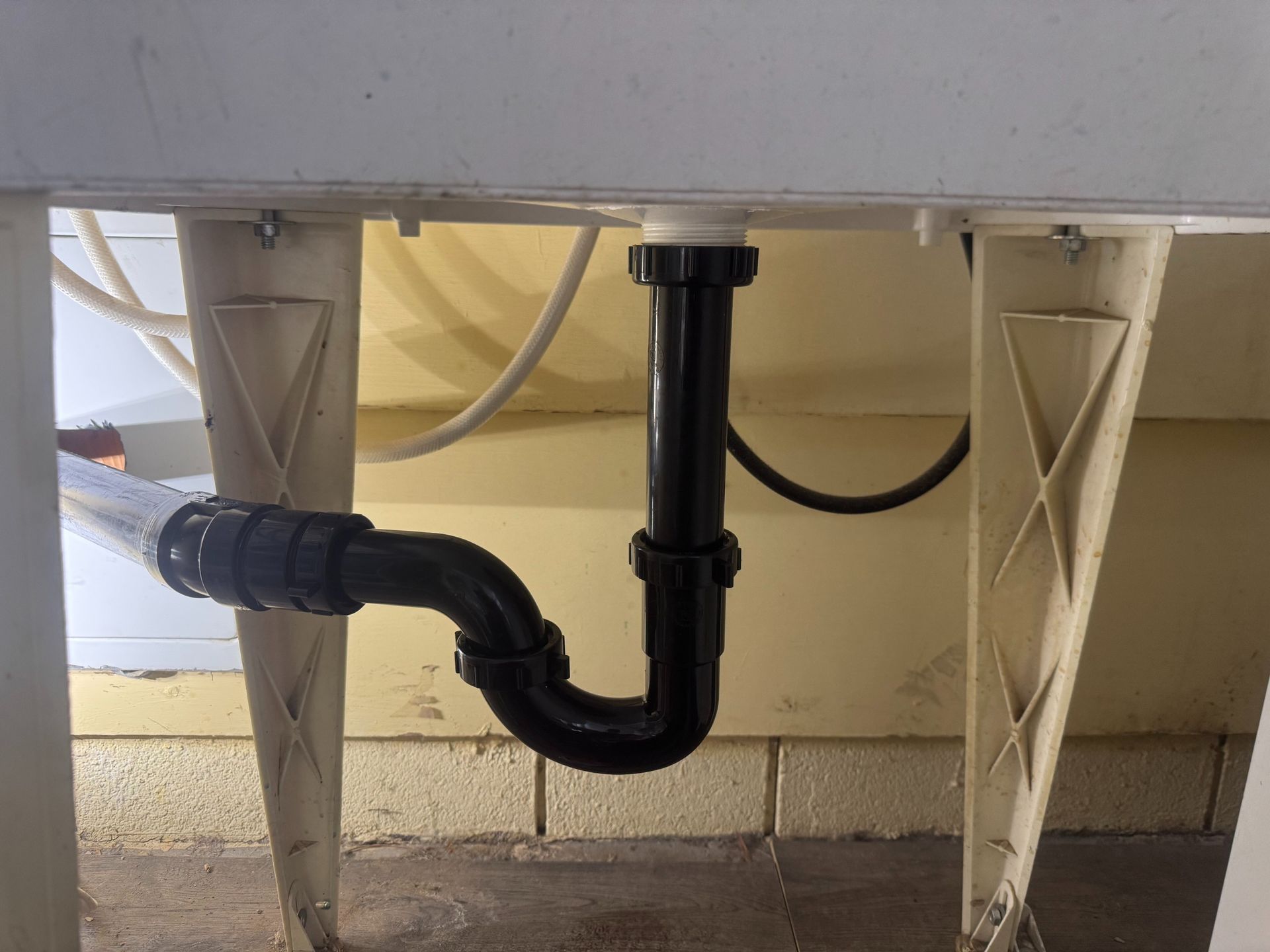 Black sink drain pipes and P-trap under a white cabinet with metal support legs