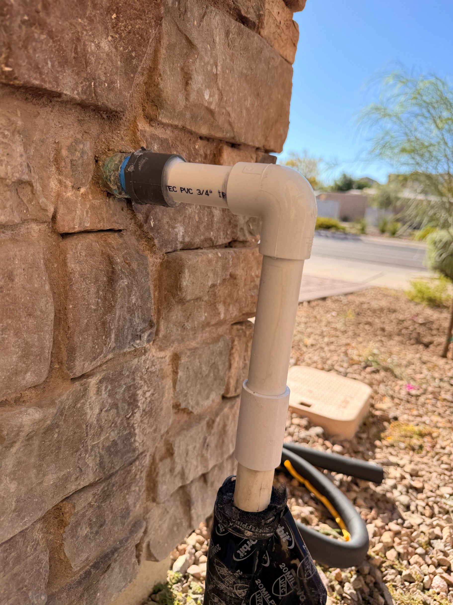 White PVC pipe connected to a stone wall, with a black base in a desert landscape.