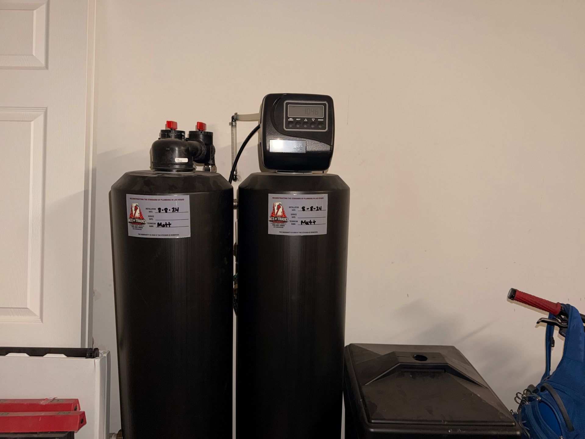 Two black water softener tanks beside a blue pressure washer in a garage-like room
