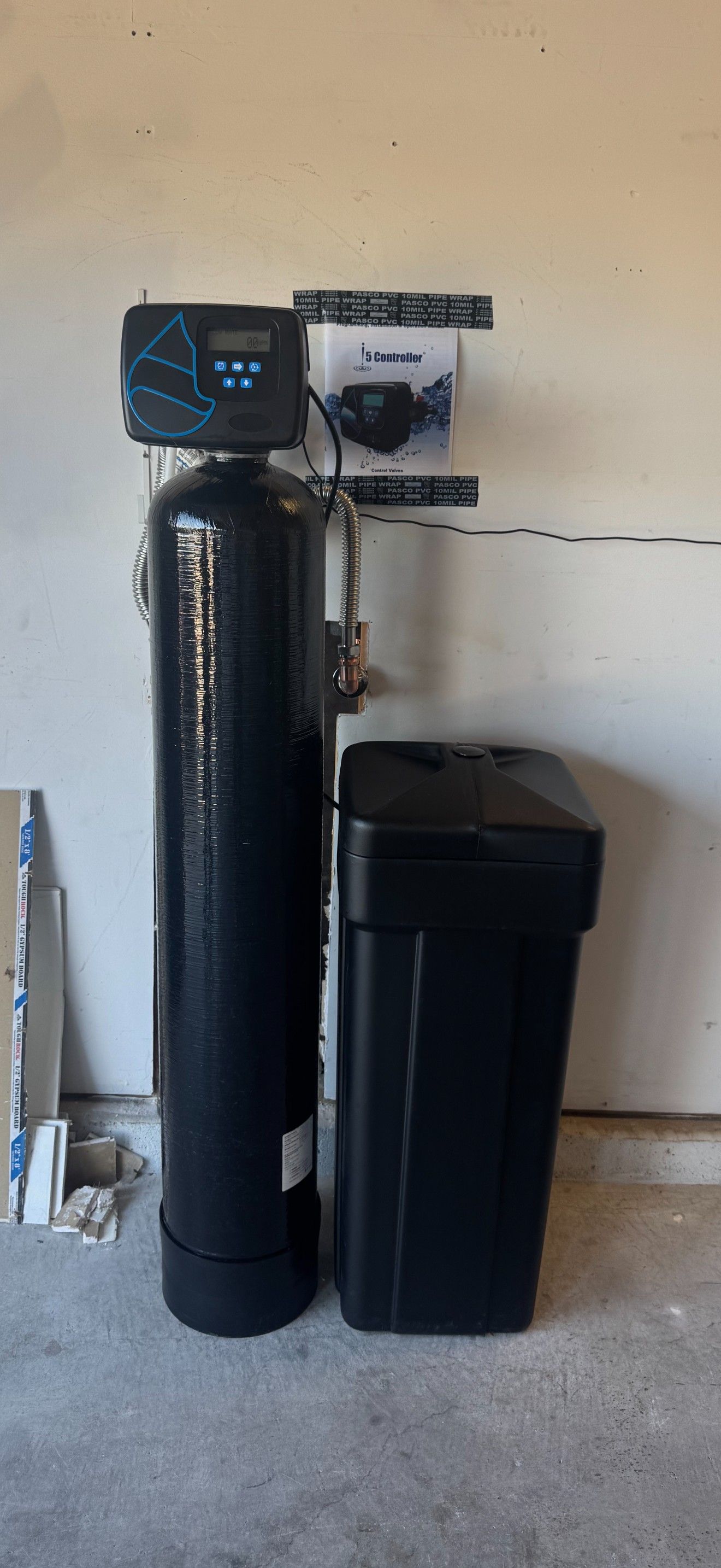 Black water softener tank and black utility cabinet against a garage wall