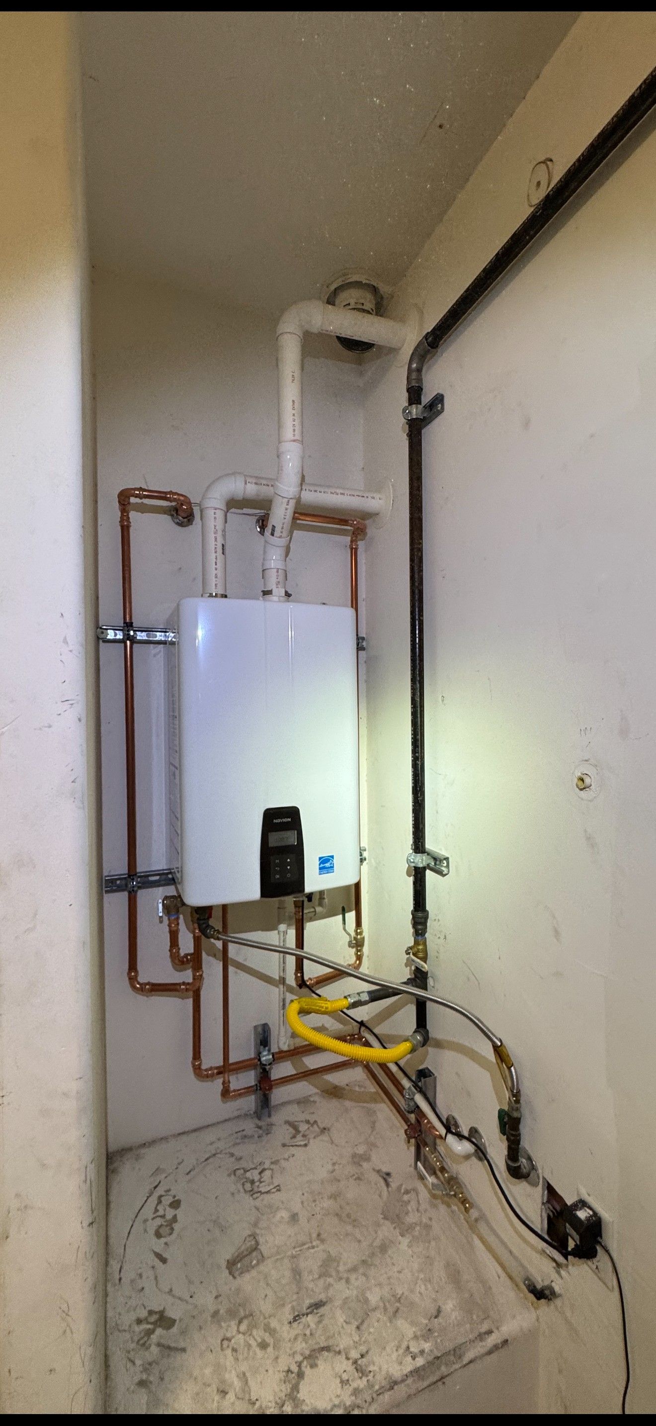 Utility closet with water heater, copper pipes, and maintenance equipment on the floor