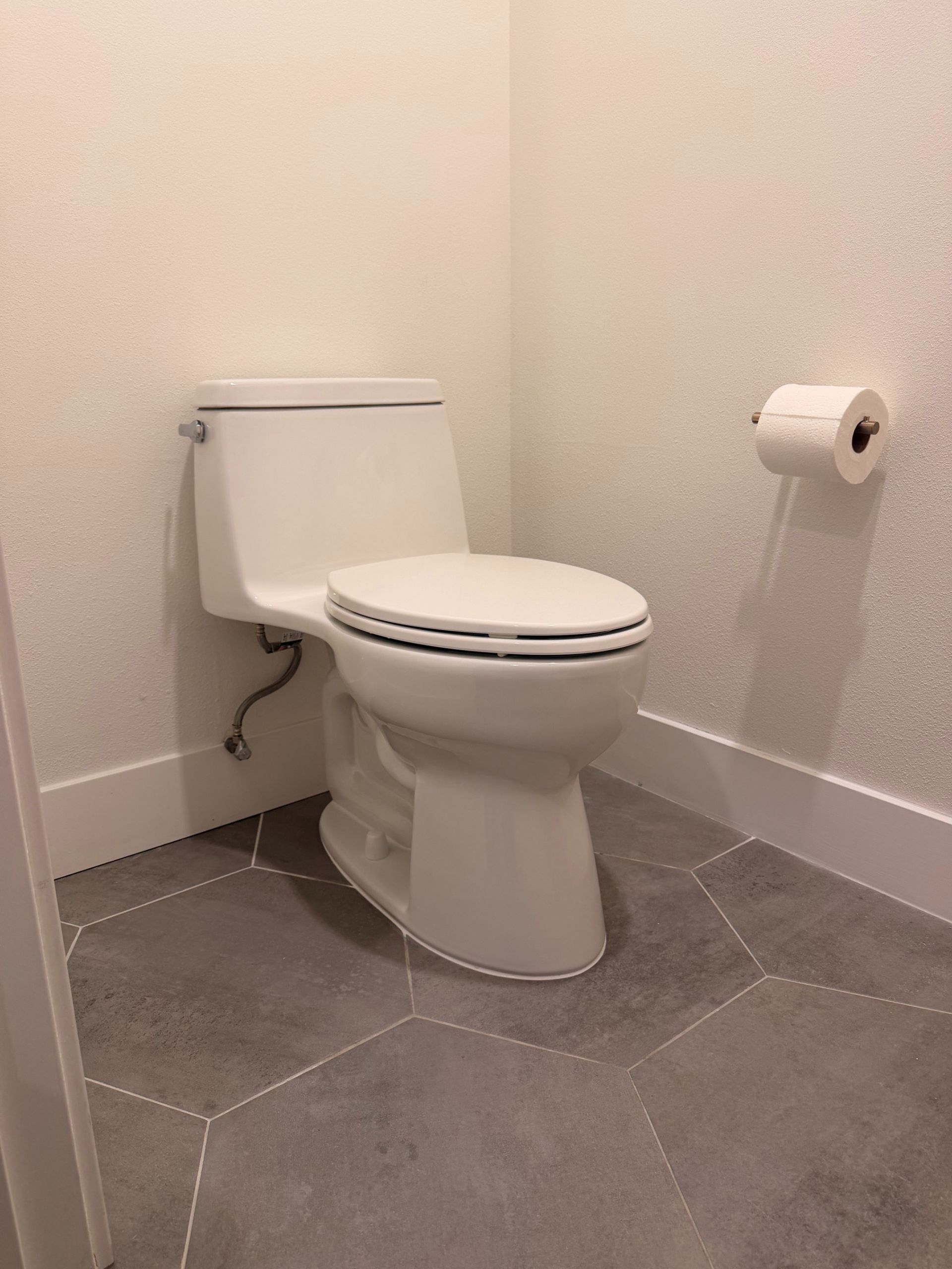 Small bathroom with a white toilet, toilet paper roll, and gray tiled floor.