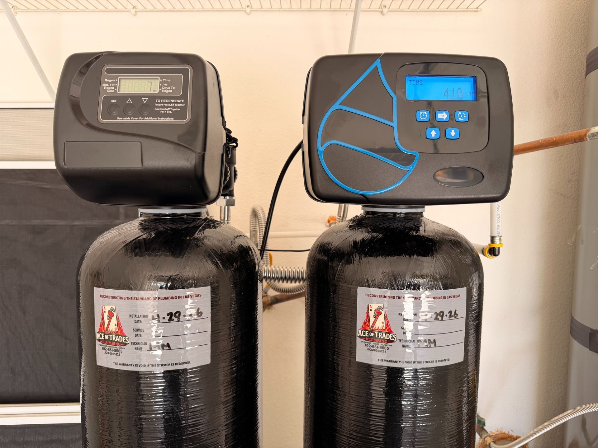 Two black water softener tanks with digital control heads in a utility room.