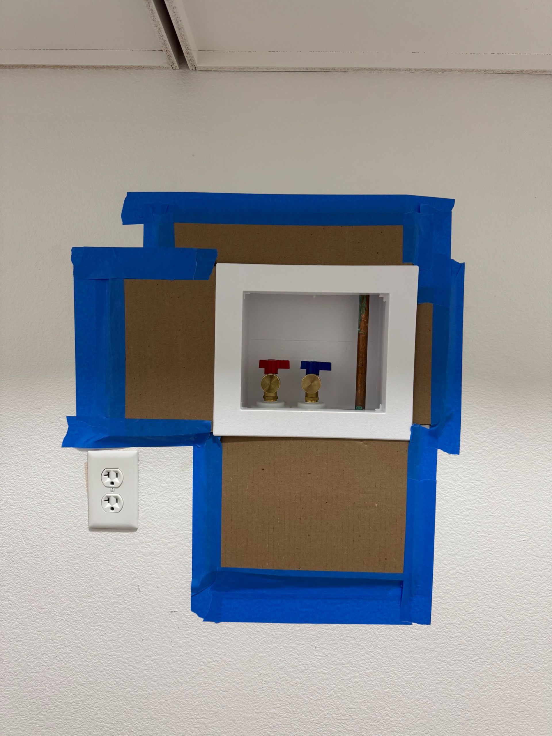 Blue-taped cardboard wall installation with a white square frame and small objects inside.