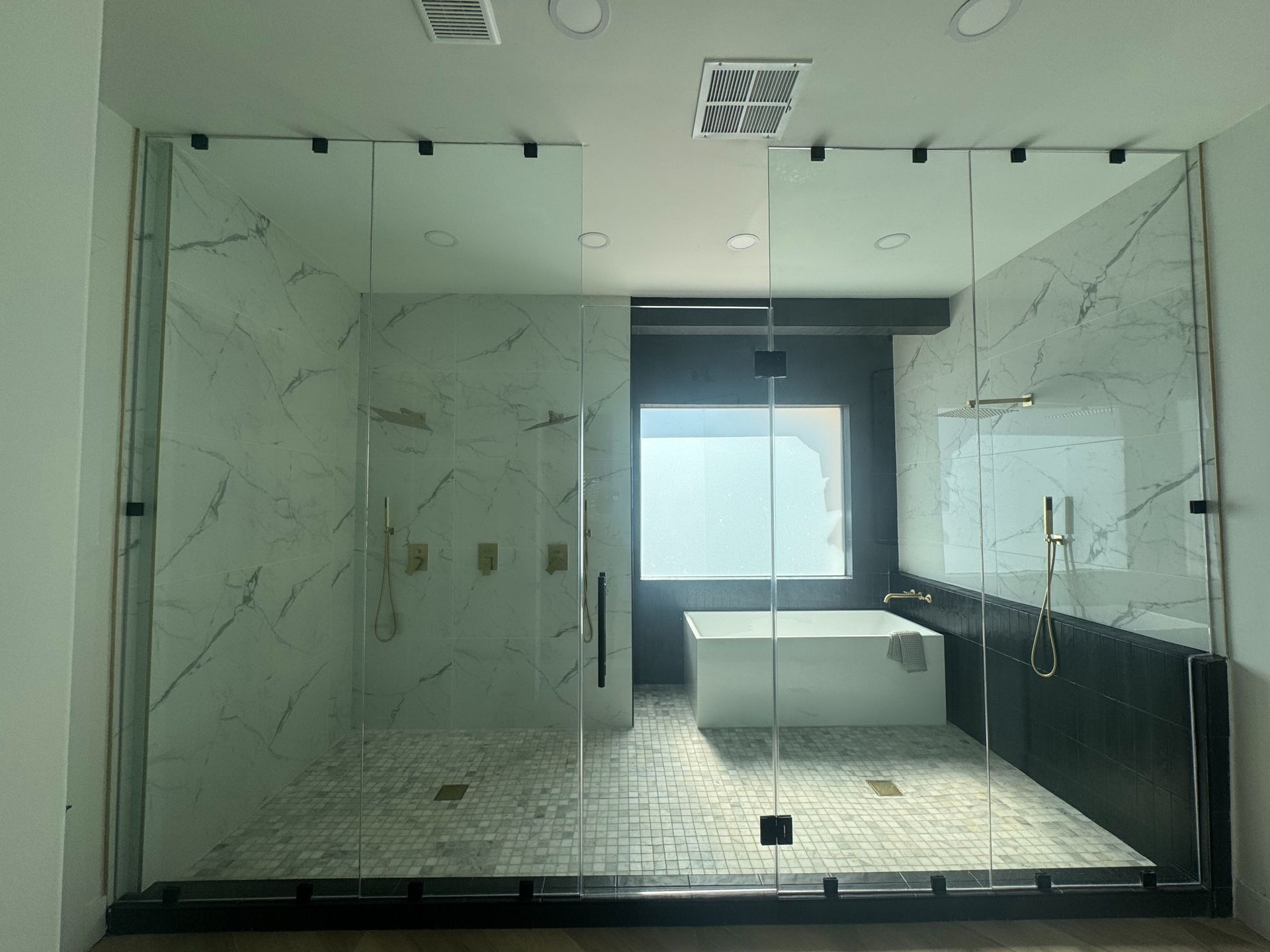 Modern bathroom with marble walls, glass shower enclosure, and black vanity beneath a window.