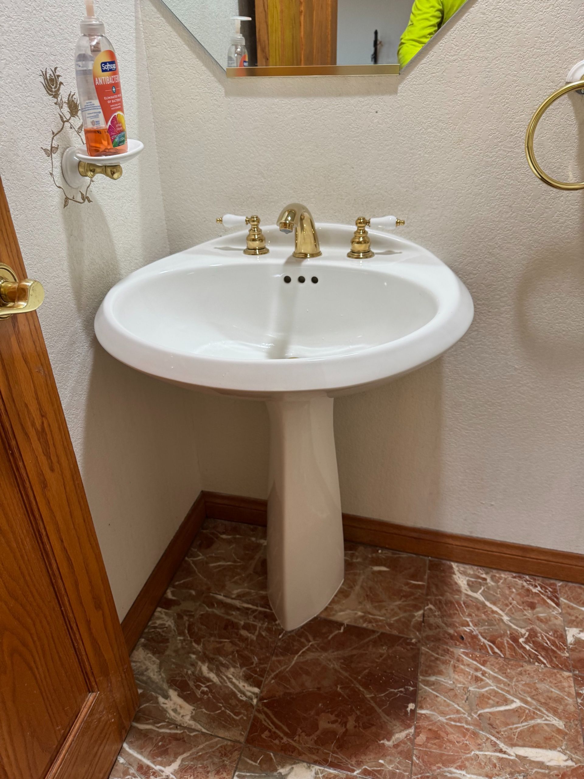 Small bathroom with white pedestal sink, brass faucet, and marble-pattern floor tiles.