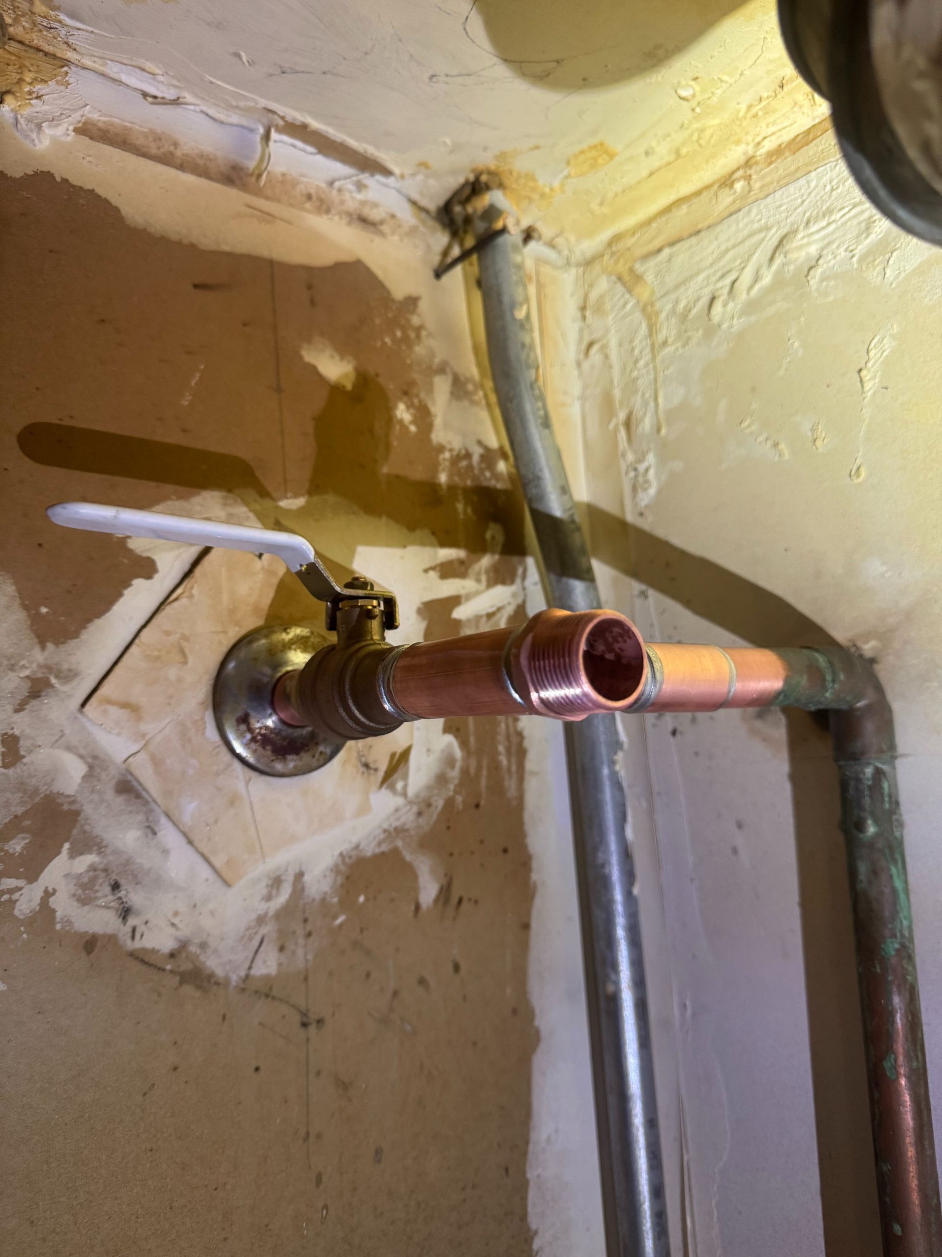 Corroded copper pipe and shutoff valve on a stained wall in a small utility area