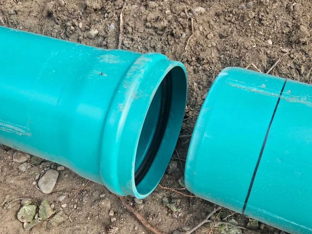 Broken turquoise pipe section lying on dirt next to a detached pipe piece