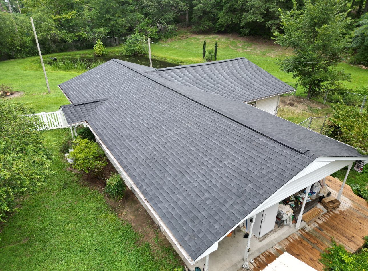 Aerial view of a house with a dark gray roof surrounded by green trees and grass