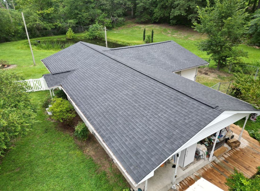 Aerial view of a house with a dark gray roof surrounded by green trees and grass