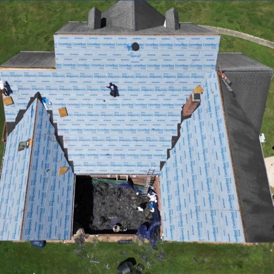 Damaged house roof with torn blue underlayment exposing a large hole over the garage.