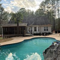 Backyard pool with white house, screened porch, and tall trees at dusk