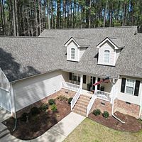 Aerial view of a suburban house with gray roof, white siding, front porch, and landscaped yard