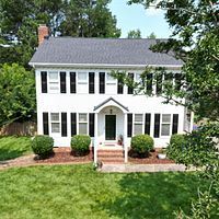 White two-story colonial house with black shutters, brick steps, and a green lawn