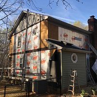 House under renovation with gray housewrap, a small ladder, and a brick chimney in a yard.