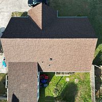 Aerial view of a house with a brown shingled roof and a small backyard with grass and patio furniture