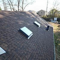 Shingled roof with several skylights and vents on a suburban house under daylight
