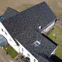 Aerial view of a house with a dark shingled roof, skylight, and satellite dish.