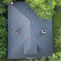 Aerial view of a gray shingled house roof with two vents and trees around it