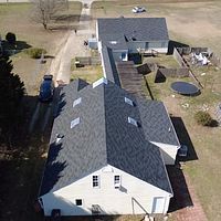 Aerial view of a white house with a dark roof, driveway, and backyard with a trampoline and shed.