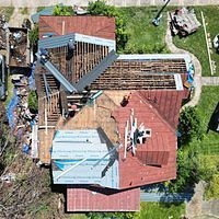 Aerial view of a damaged house with a partially collapsed red roof and exposed beams.