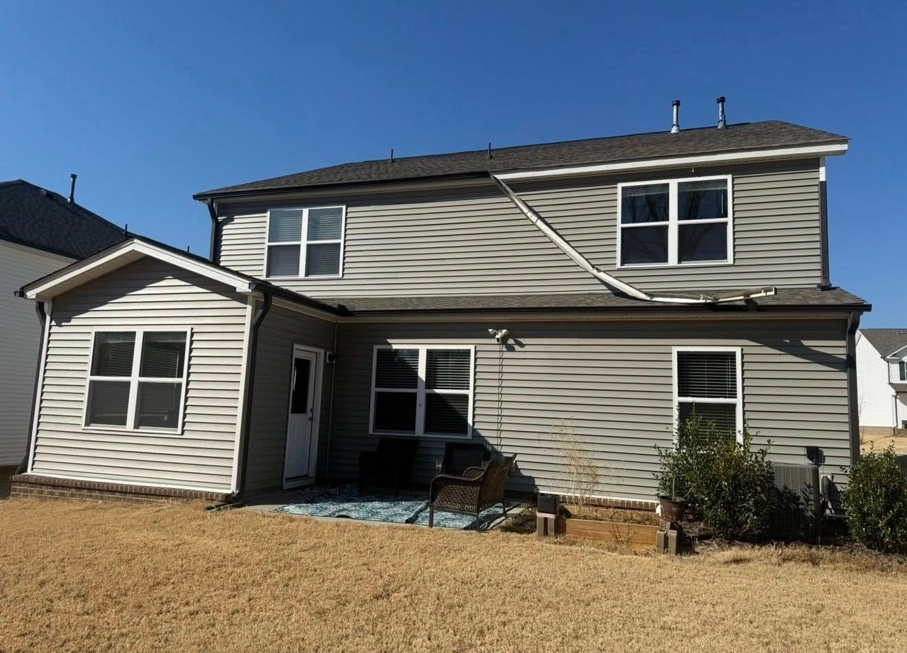 Two-story gray house with white trim and a small side extension under a clear blue sky