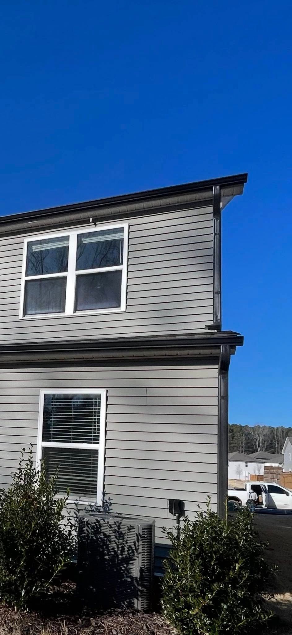 Gray two-story house exterior with white-trimmed windows under a blue sky