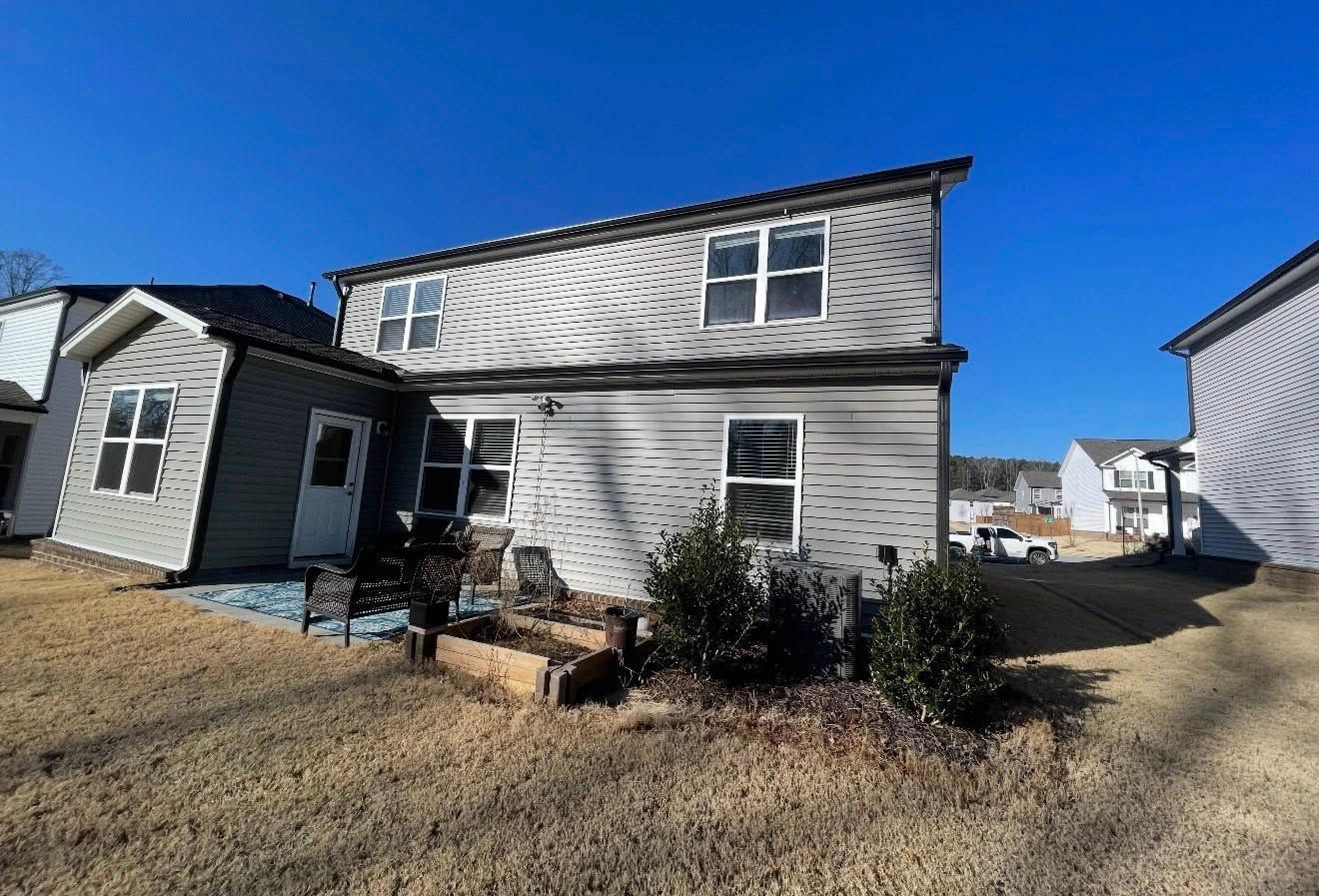 Two-story gray house with a small front porch and shrubs under a bright blue sky.