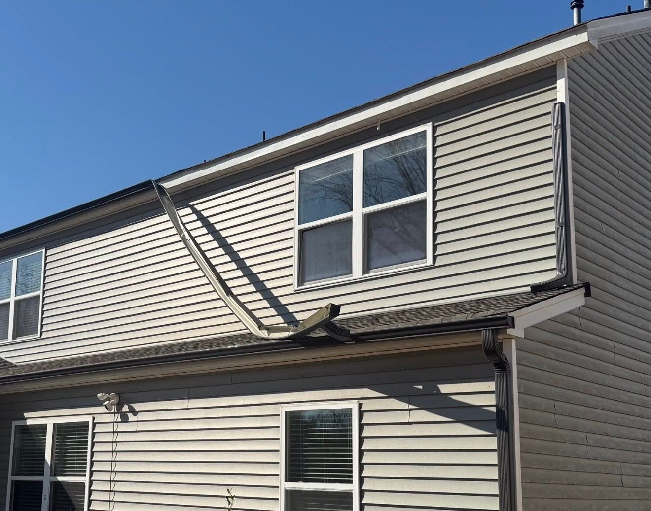 Damaged roof gutter and siding on a beige townhouse exterior under a clear blue sky