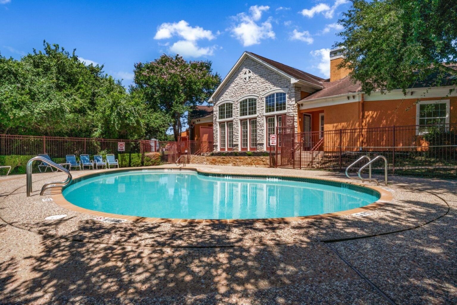 Backyard with a turquoise swimming pool beside a brick house under a blue sky