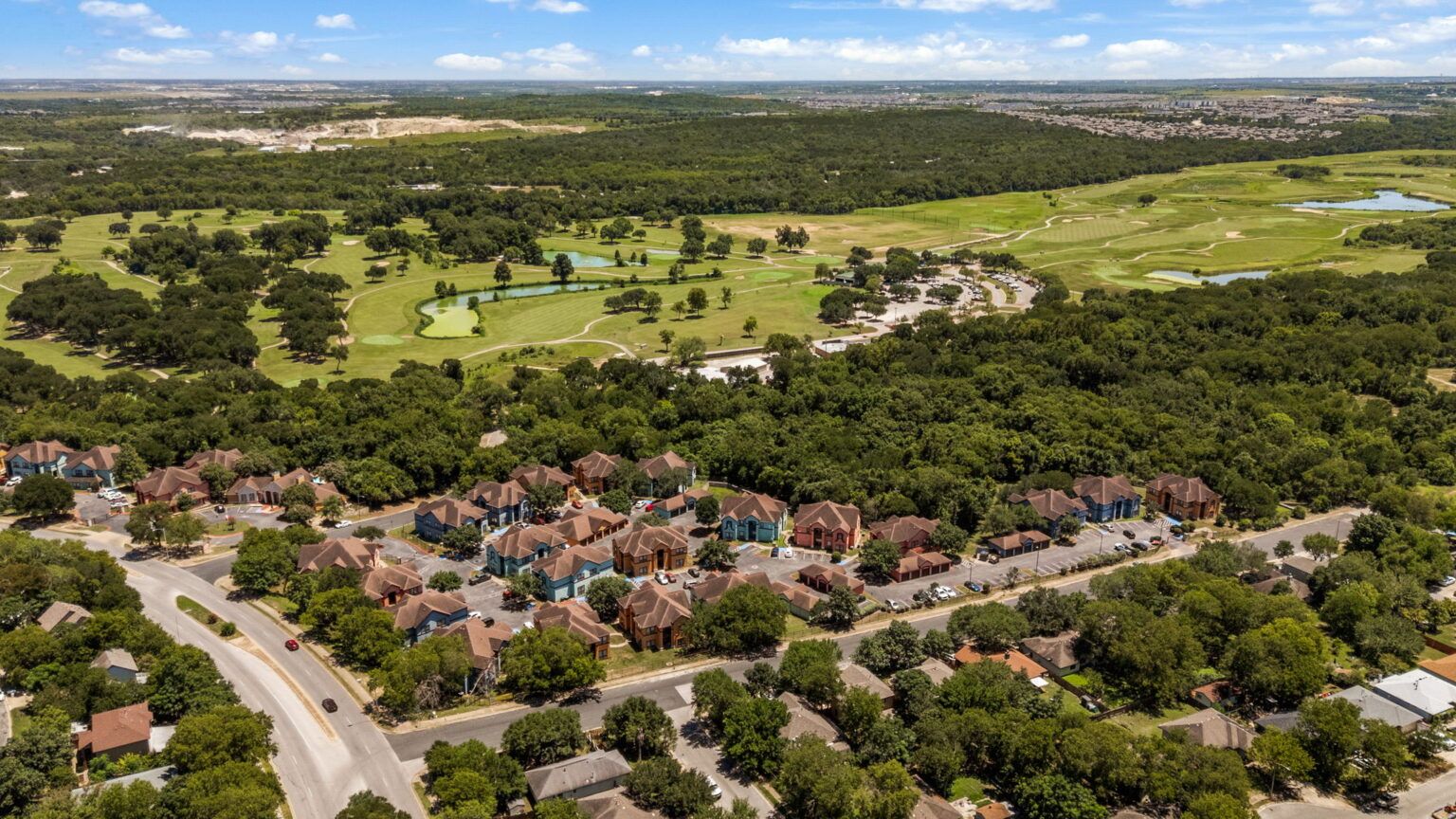 Aerial view of a suburban neighborhood beside a green golf course and wooded landscape