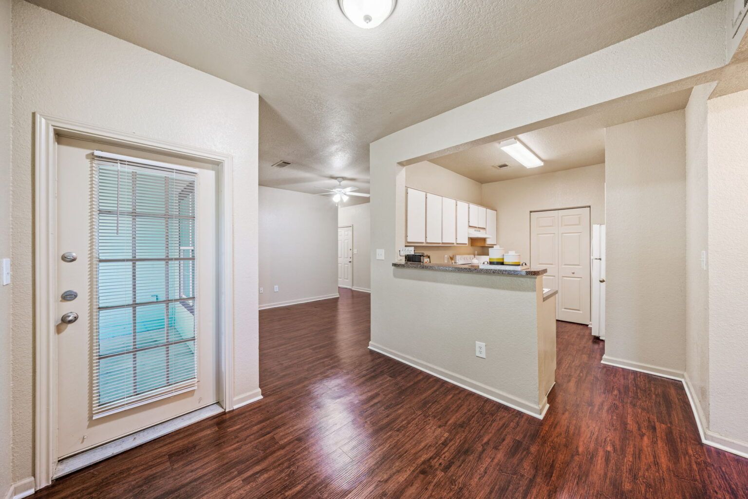 Empty open-plan living area with wood floors, white walls, and a kitchen pass-through.